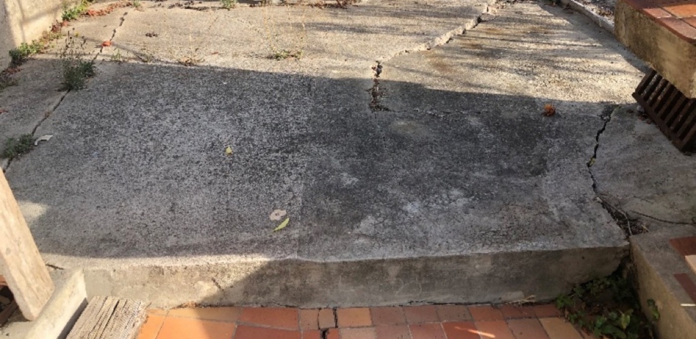 Terrasse en béton fissurée et affaissée au-dessus d'un mur de soutènement qui bascule